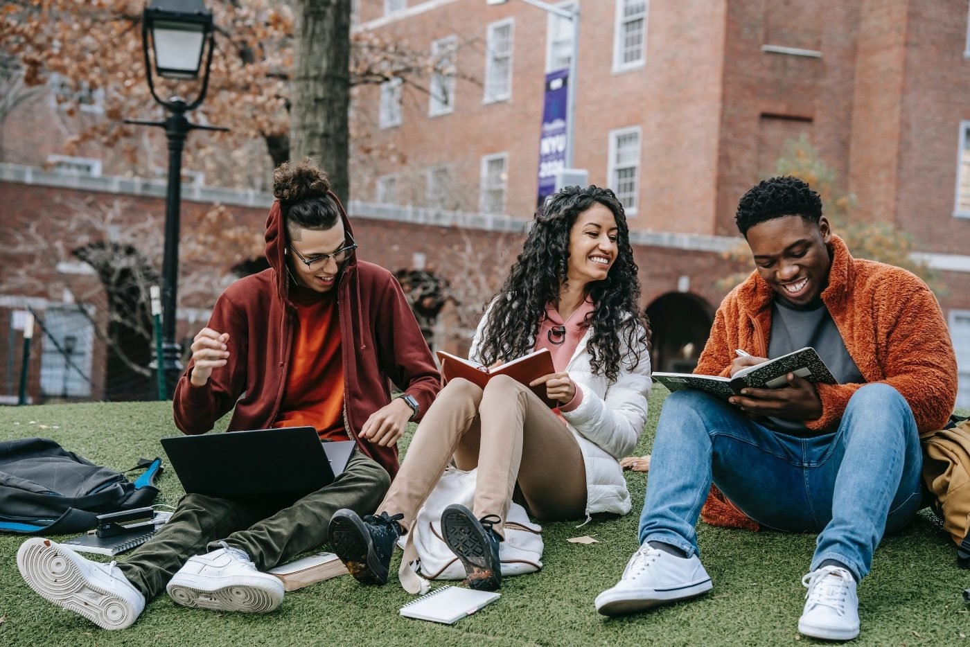 Students sitting together on a campus lawn with notebooks and laptops